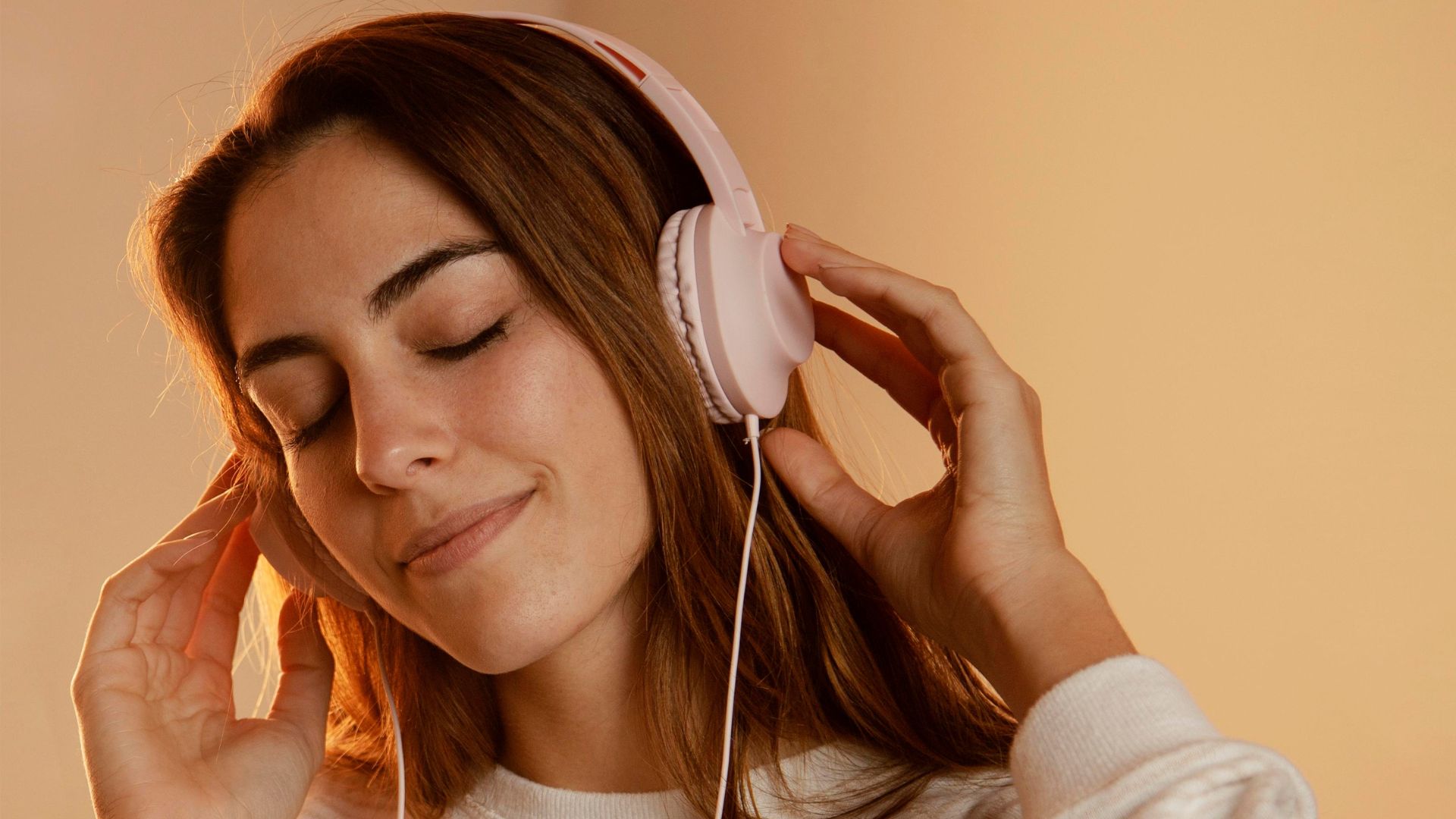 Młoda kobieta ma założone różowe słuchawki na uszach i słucha muzyki.