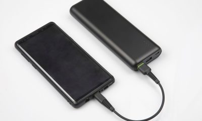 Czarny powerbank do telefonu ładuje go poprzez kabel USB na białym blacie.