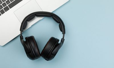 Czarne słuchawki leżą obok laptopa na niebieskim blacie.