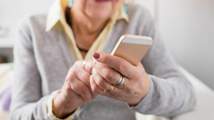 Starsza kobieta trzyma w dłoniach nieduży smartfon dla seniora.