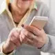 Starsza kobieta trzyma w dłoniach nieduży smartfon dla seniora.